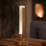 Stämningsfull bordslampa i mässing och glas från Örsjö Belysning, placerad på ett trägolv i varm inomhusmiljö.